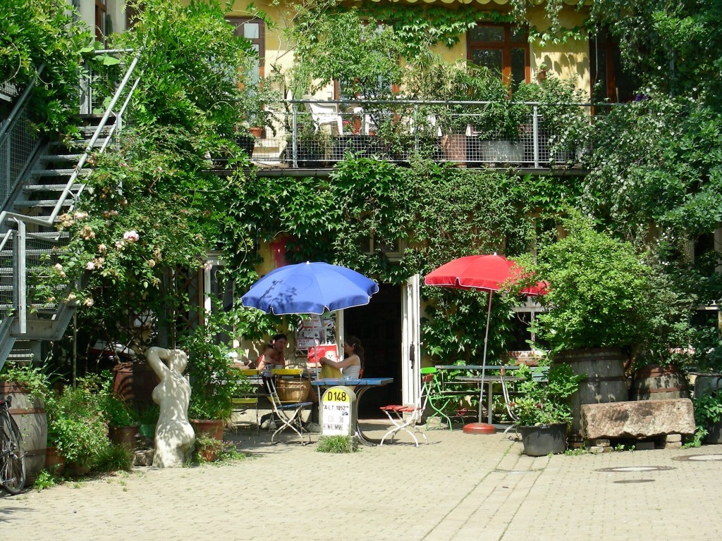 freier Blick aufs Sommerlich zugewachsene Strandcafe mit ausgeklappten Schirmen als idyllischer großer Innenhof